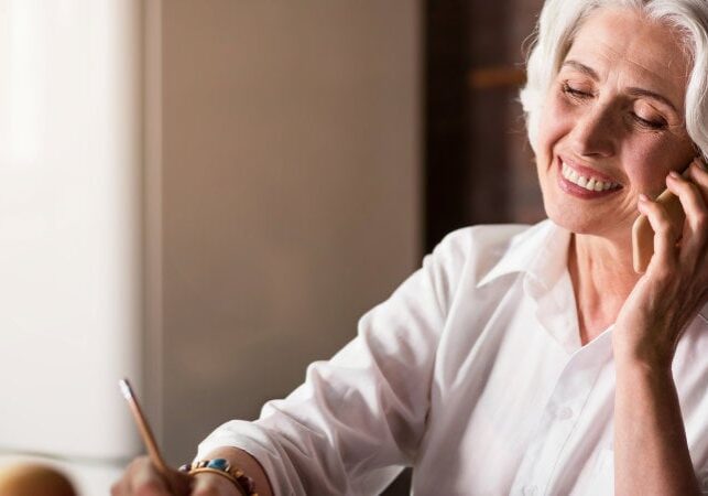 Smiley. Pleasant old lady communicating with her family and friends using telephone and laptop